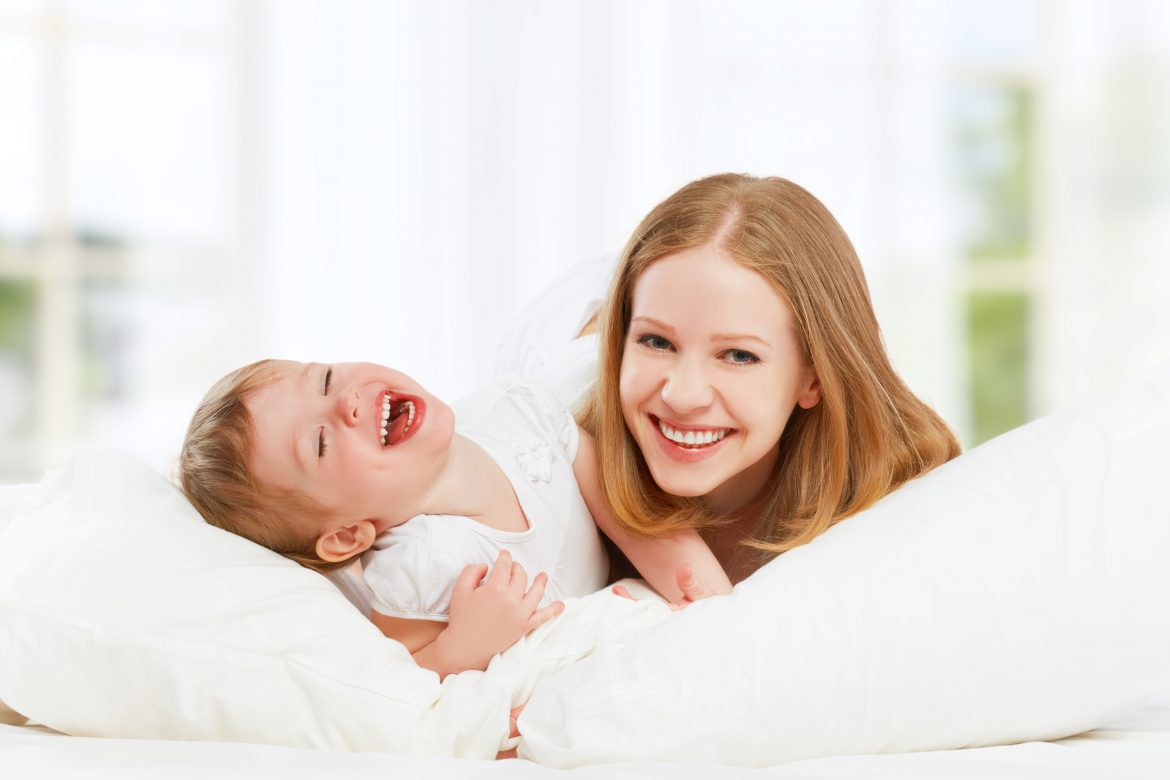 The happy family mother and baby daughter playing and laughing baby kissing in bed